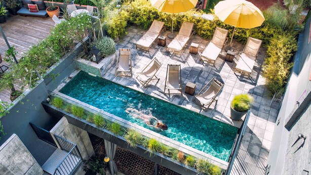 Pool på taget med liggestole og parasoller, omgivet af grøn vegetation og en træterrasse.