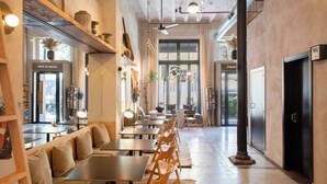 En rummelig café med træborde og bænke, et højt loft med synlige bjælker, og store vinduer der lukker naturligt lys ind.