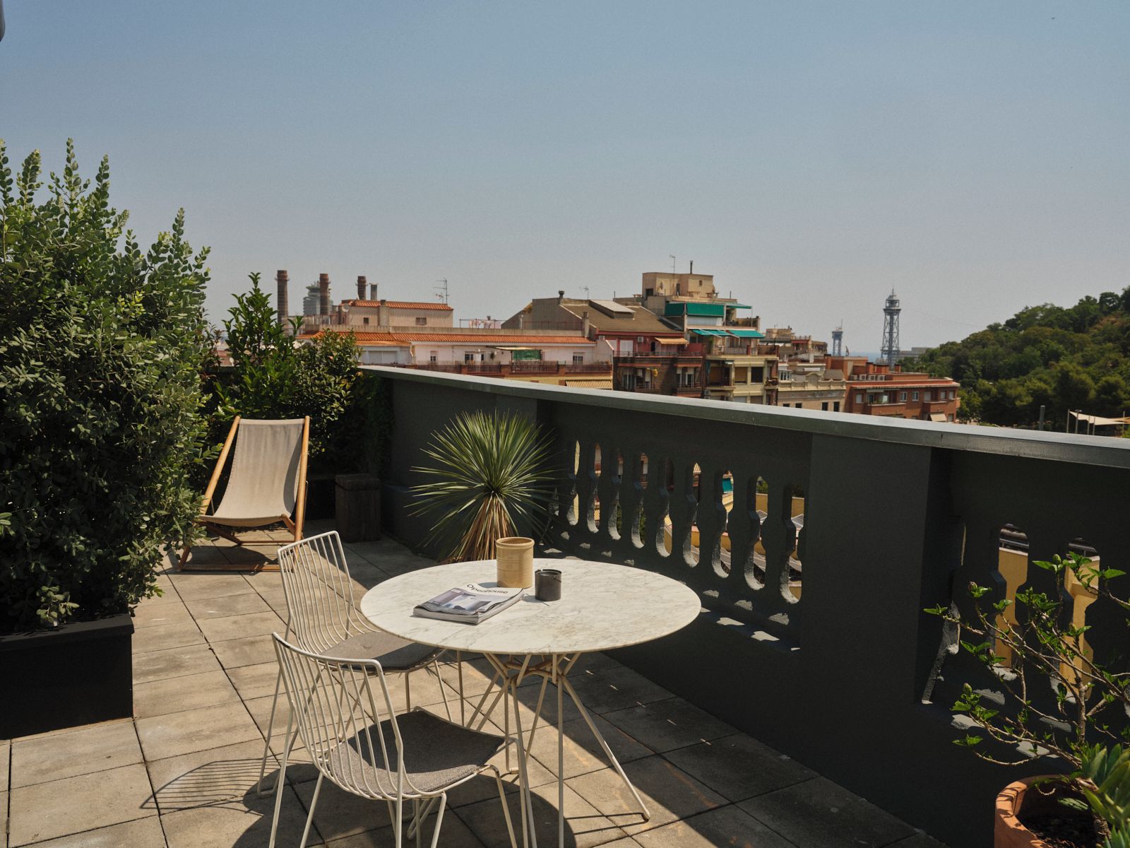 A rooftop terrace with a round table, two chairs, and potted plants.
