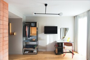 A modern room with a wooden floor, a black TV mounted on the wall, a desk with a chair, and a clothing rack with hanging clothes. - Hotel Brummell (Barcelona)