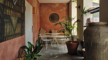 Un rincón interior acogedor con un sofá y sillones, rodeado de macetas y un jarrón grande.