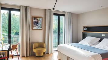 Una habitación de hotel con una cama, una silla, un escritorio con computadora y un gran ventanal con cortinas.