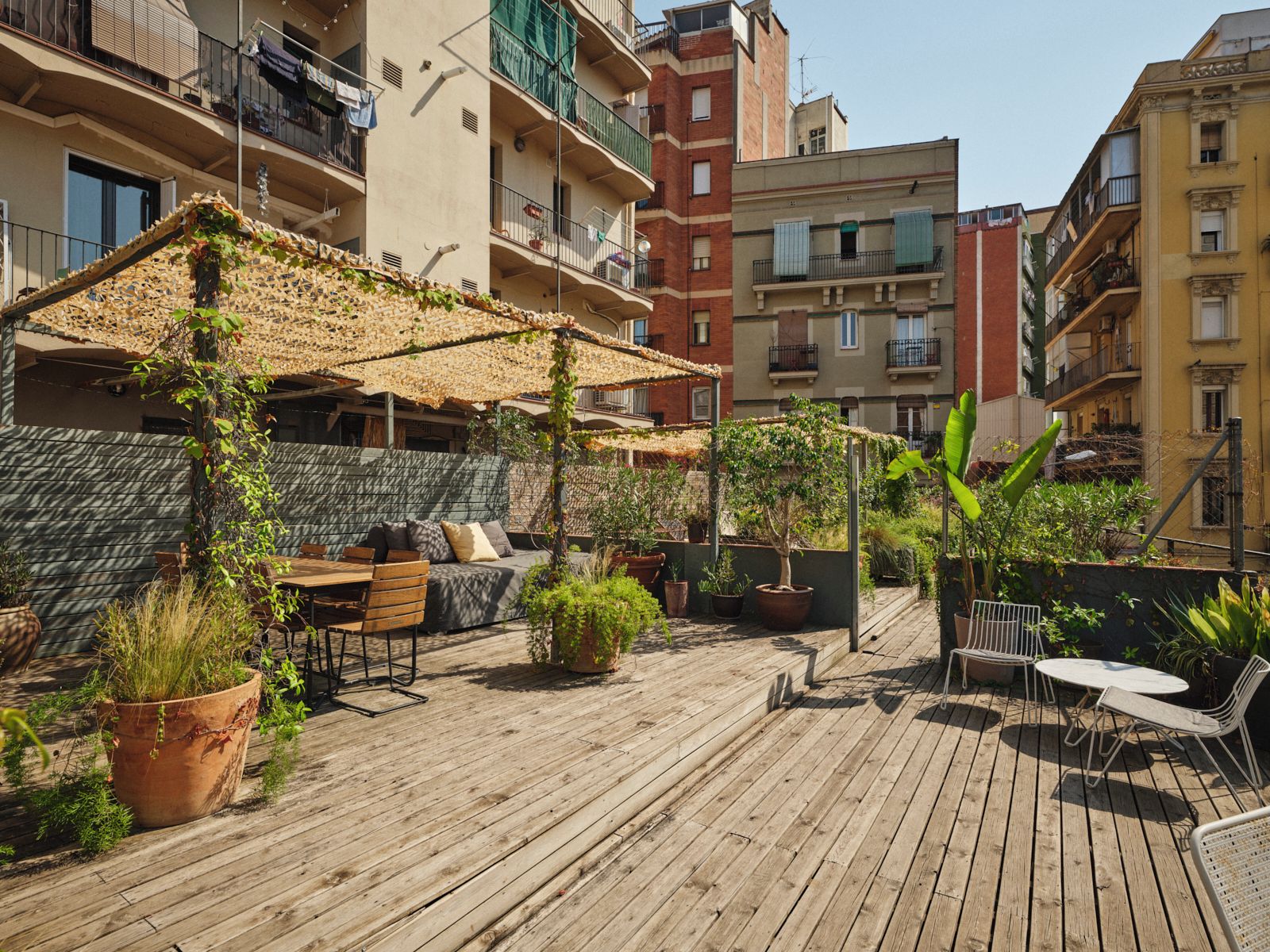 Una terraza de madera con mobiliario exterior, plantas en macetas y una pérgola con techo de paja.