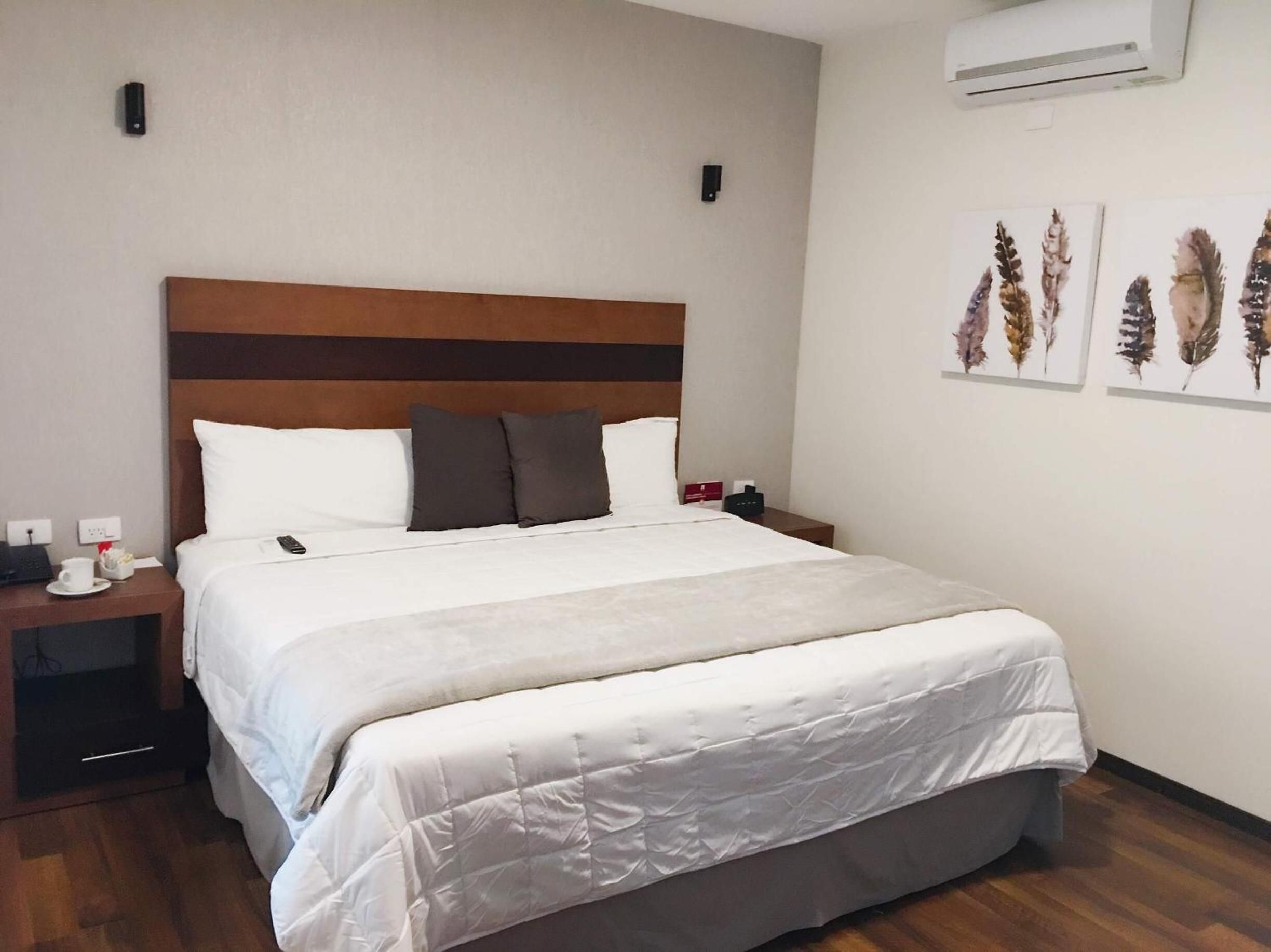 Quarto de hotel com cama, mesa de cabeceira, aparelho de ar condicionado e obras de arte nas paredes.
