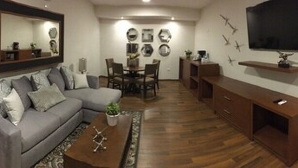 Una sala de estar con un sofá gris, una mesa de centro, un televisor y un comedor con sillas y una mesa.