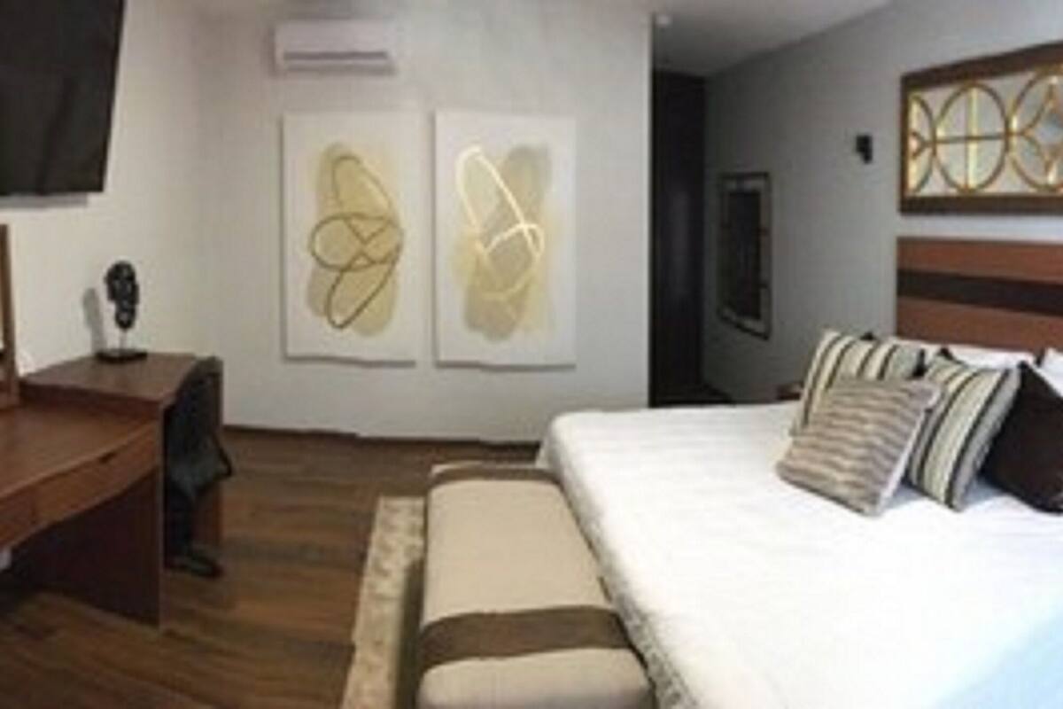 A hotel room with a bed, bedside table, dresser, mirror, artwork on the walls, and a television mounted on the wall.