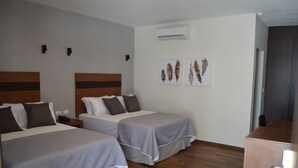 Habitación de hotel con dos camas, piso de madera, equipo de aire acondicionado y obras de arte en la pared.