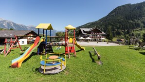 A playground with slides and climbing structures, surrounded by a grassy area and a mountain backdrop. - Seiterhof (Schladming)