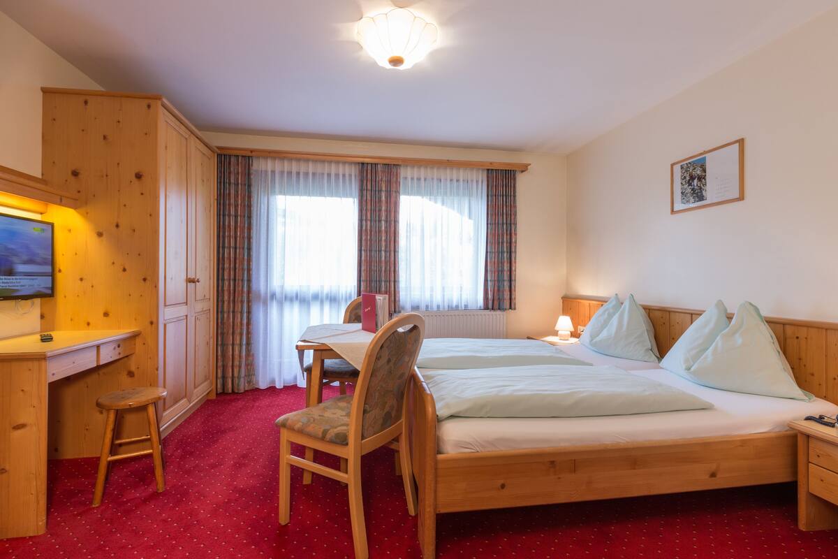A hotel room with a wooden bed, a desk with a chair, a television, and a window with curtains.