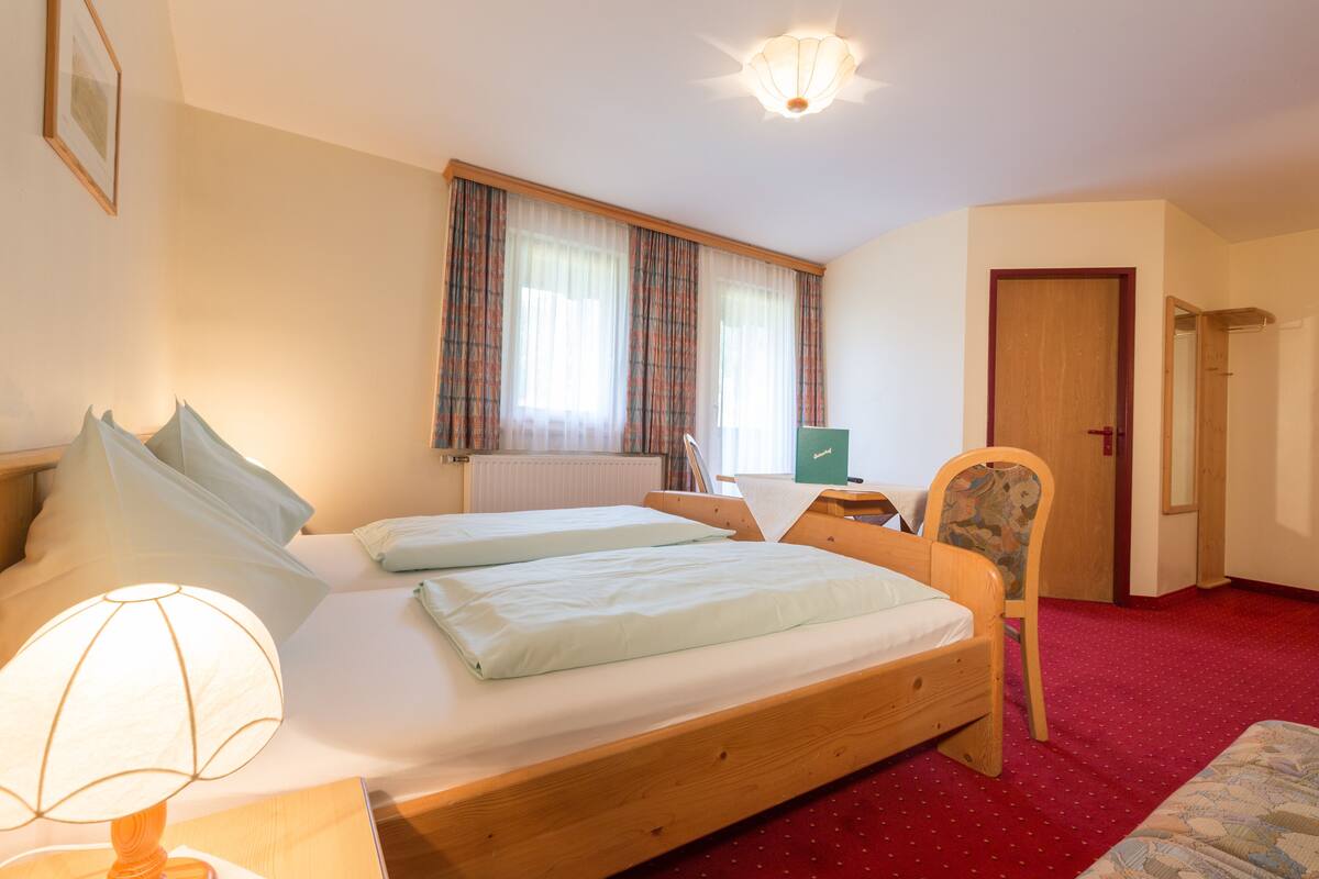 A bedroom with two beds, a desk, a chair, a lamp, and a window with curtains.