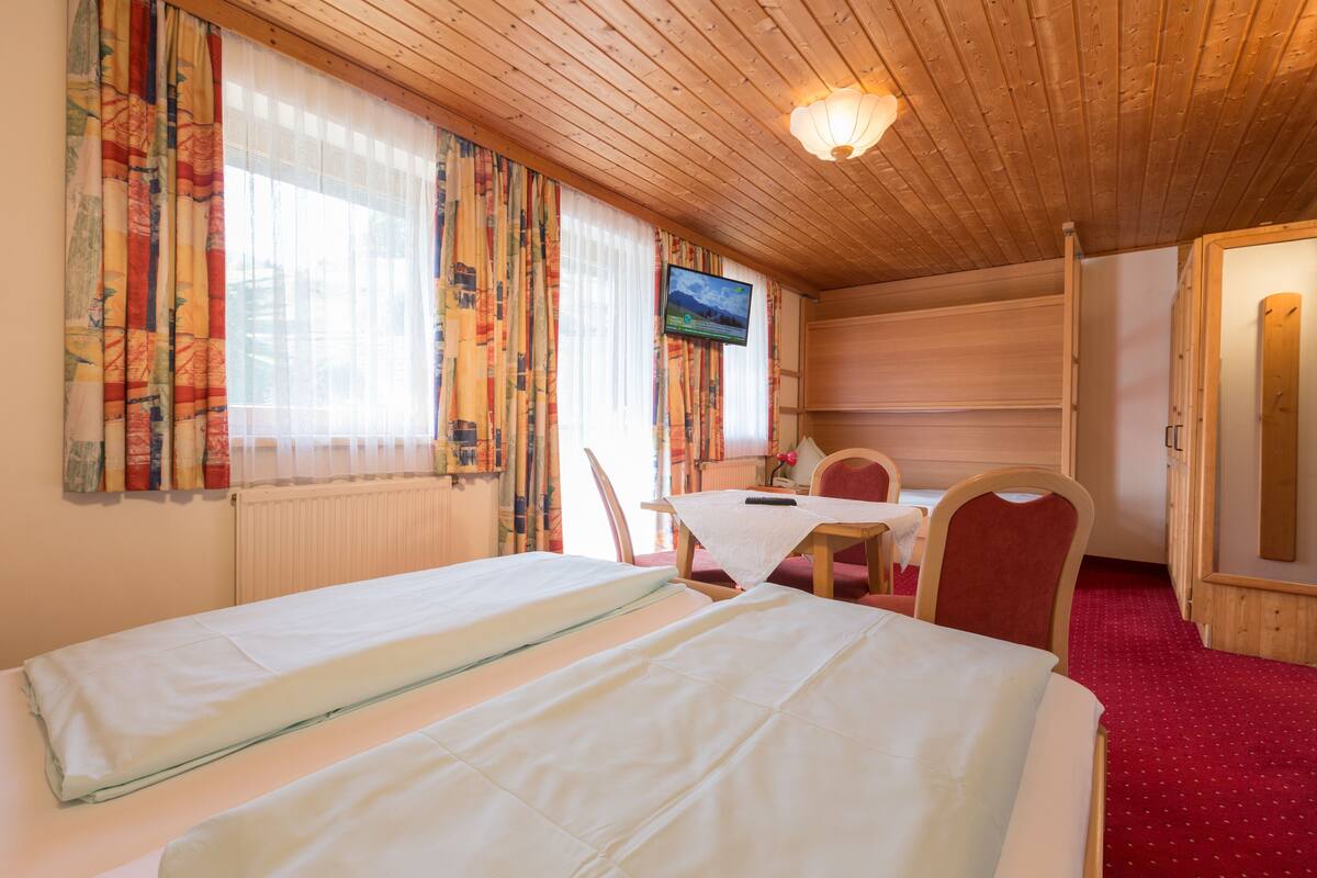A hotel room with two beds, a television, a table, and a red carpet.