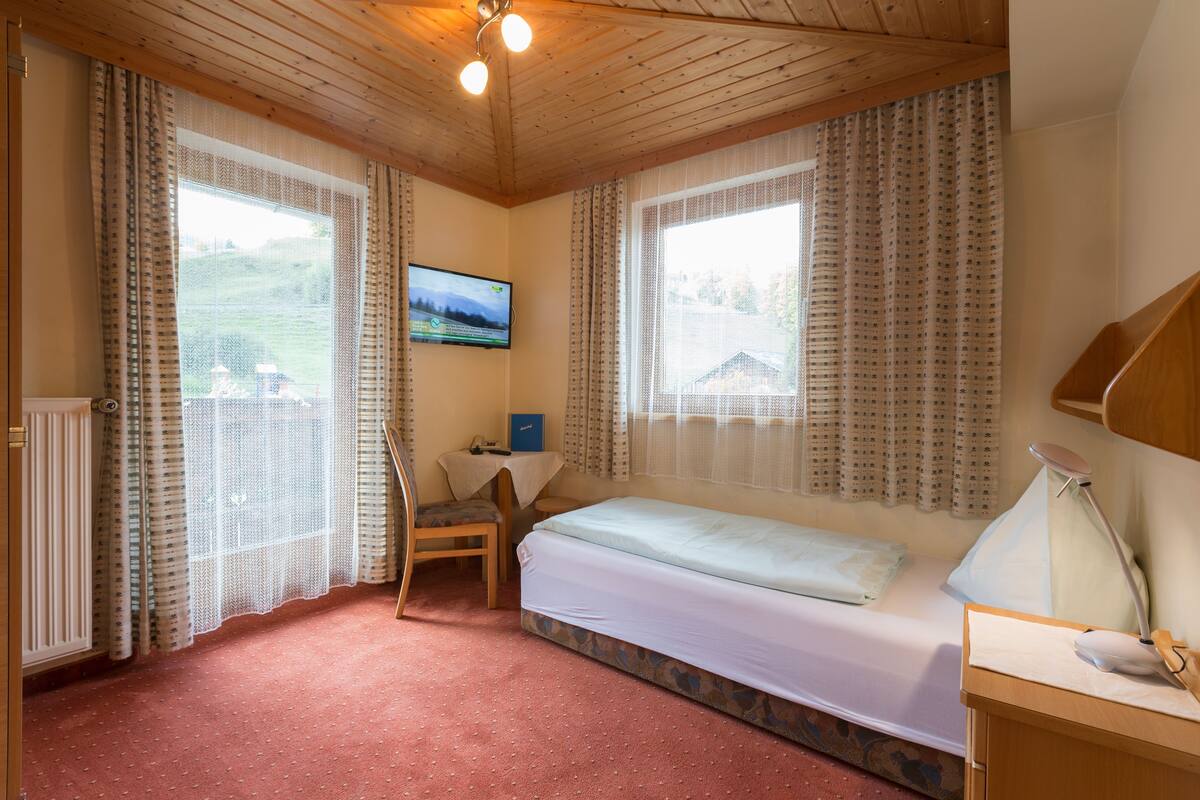 A bedroom with a bed, a desk, a chair, a TV, and curtains.
