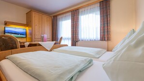 A hotel room with two beds, a TV, a desk, and a window with curtains. - Seiterhof (Schladming)