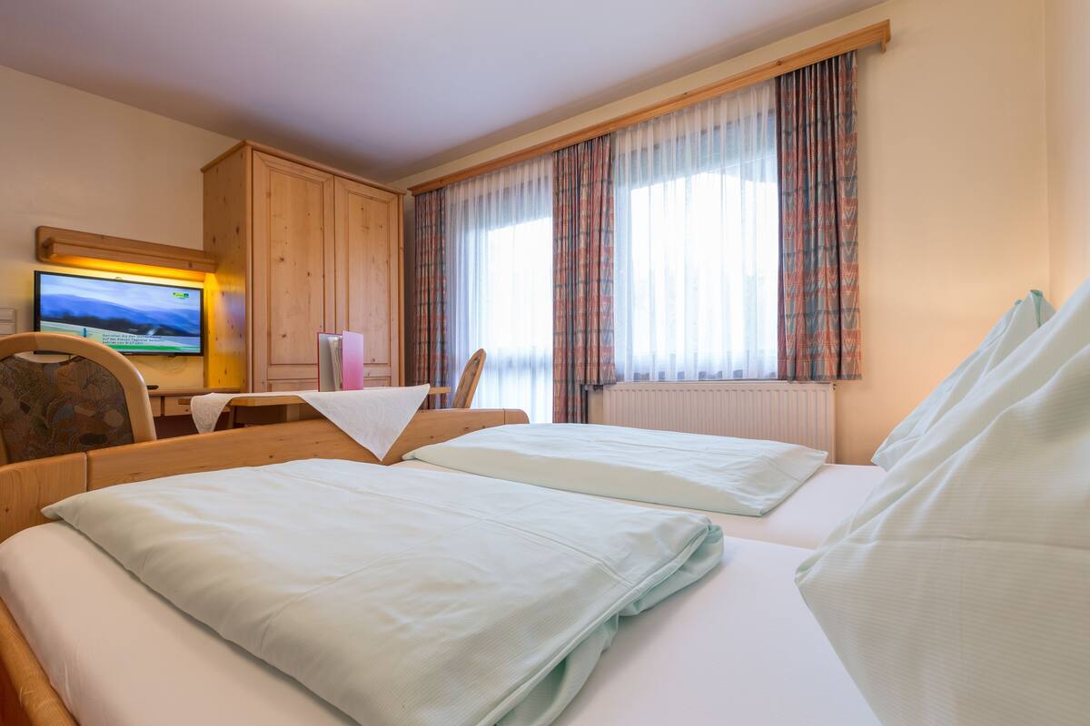 A hotel room with two beds, a TV, a desk, and a window with curtains.
