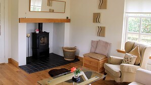 A cozy living room with a fireplace, a sofa, a glass coffee table, and a wicker basket. - Westacre Lodge Self Catering Chalet (Crieff)