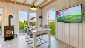 Een eetruimte met een tafel, stoelen, een aan de muur bevestigde televisie en een houtkachel.