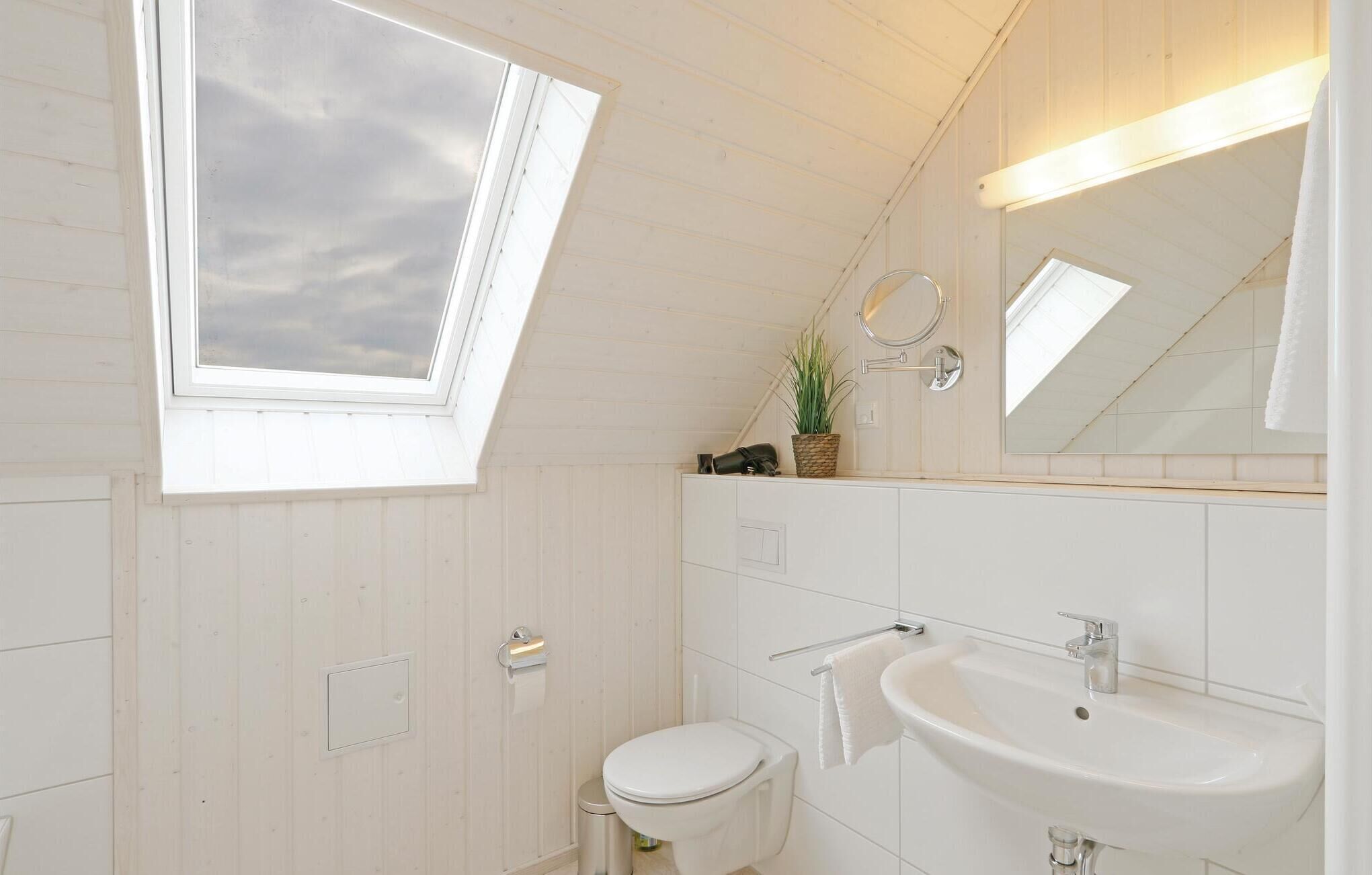 Een moderne badkamer met dakraam, toilet, wastafel en spiegel.