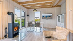 Een knus vertrek met een houtkachel, een eethoek met stoelen, een rieten bank en een aan de muur bevestigde televisie.