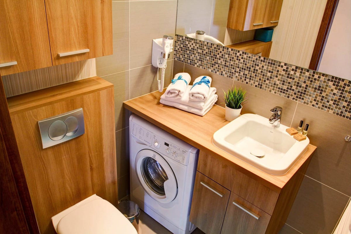 A compact bathroom with a washing machine, a sink, and a mirror.