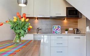 A modern kitchen with white cabinets, a stainless steel sink, and a colorful table runner. - Marina Jastarnia  - Apartamenty - Basen (Jastarnia)