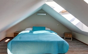 A bedroom with a sloped ceiling, a bed with a blue bedspread, a nightstand, and a small wooden cabinet. - Marina Jastarnia  - Apartamenty - Basen (Jastarnia)