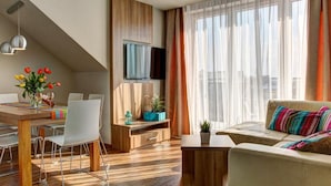 Un salon moderne comprenant un coin repas, un plancher en bois, un téléviseur à écran plat et une grande fenêtre avec des rideaux.