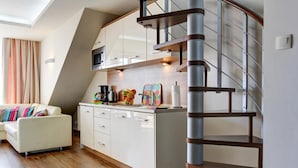 Une cuisine moderne avec des meubles blancs, un escalier en bois et un coin repas comprenant une table et des chaises blanches.