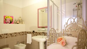 A bathroom with a white sink, a bidet, a toilet, a mirror, and a decorative metal chair with a pink towel and a rose. - Easy Dream Rooms (Verona)