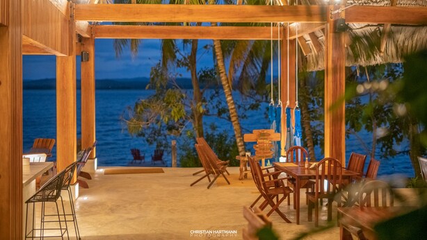 Un área de comedor al aire libre con muebles de madera y vista al océano al atardecer.