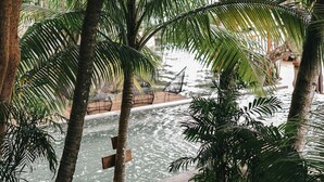 Un área junto a la piscina con palmeras y una estructura de techo de paja.