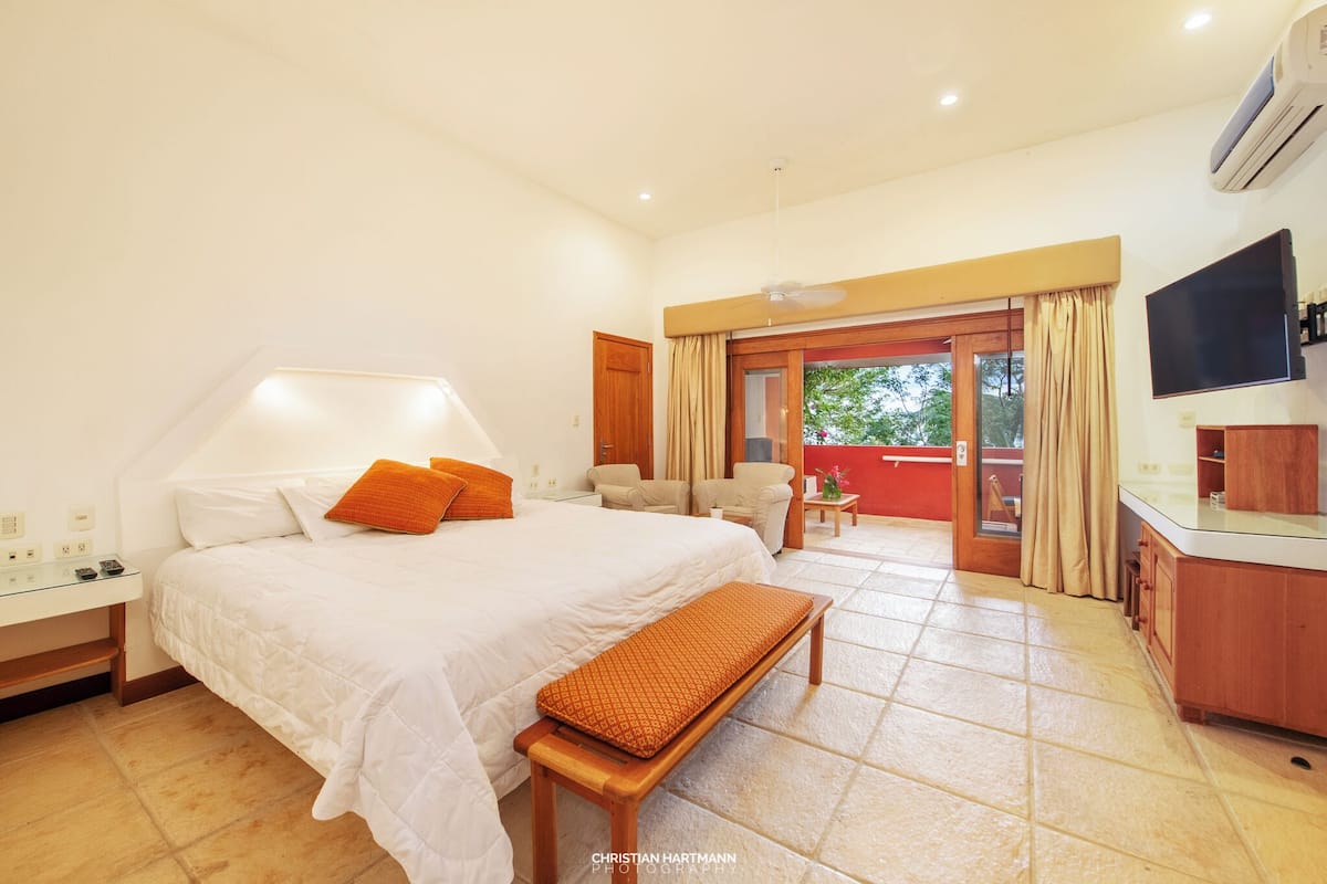 Habitación de hotel con cama, mesita de noche, banco y vistas al exterior.