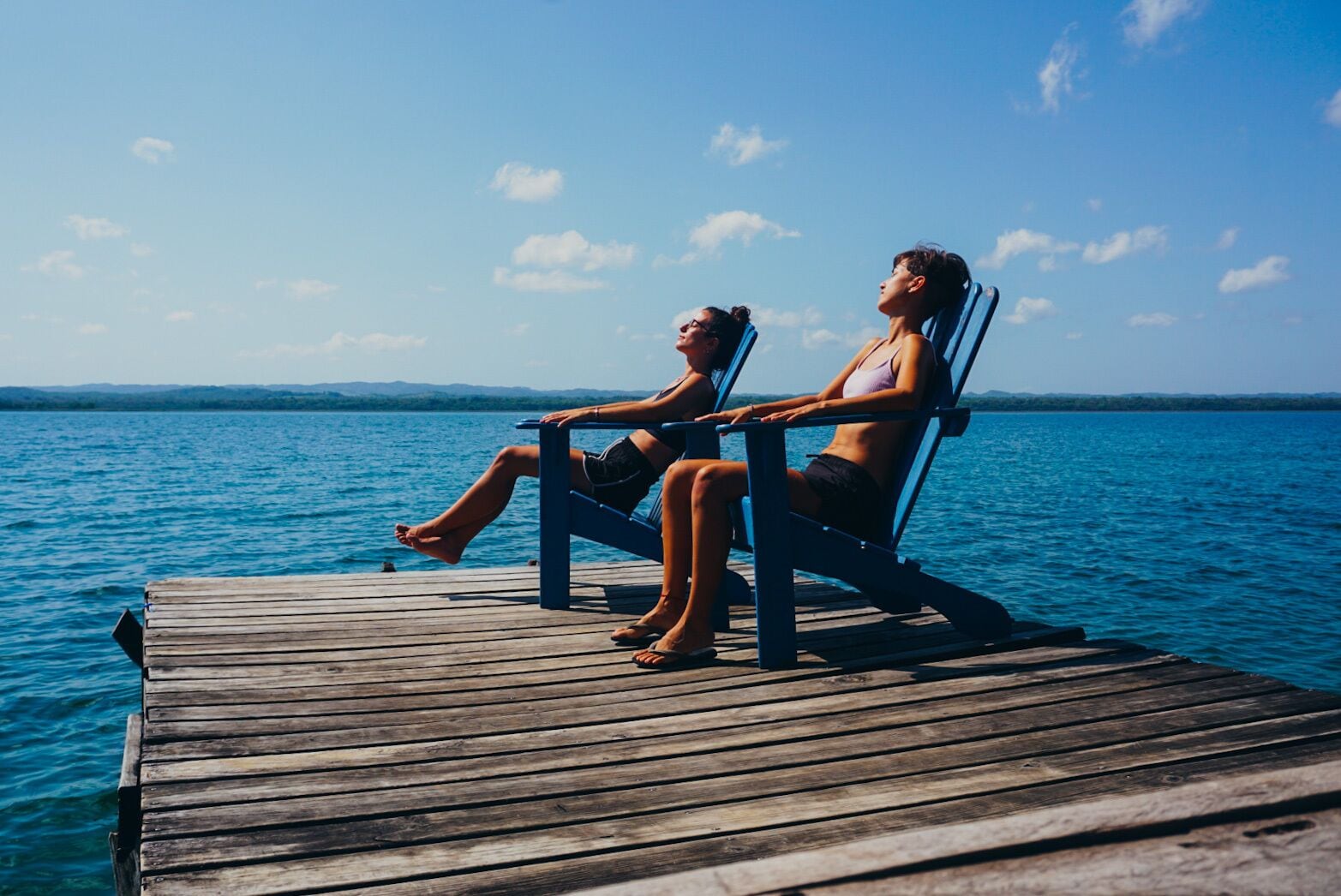 Dos personas sentadas en un muelle de madera junto a un cuerpo de agua.