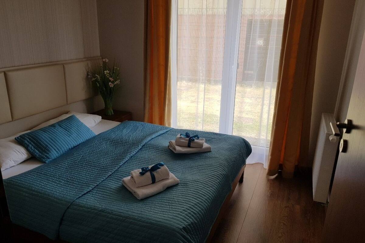 Ein Hotelzimmer mit Bett, Nachttisch, einem Fenster mit Vorhängen und einer Heizung.