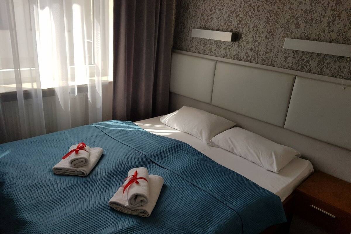 Ein Hotelzimmer mit Bett, zwei Handtüchern mit roten Bändern, einem Nachttisch und einer Wandleuchte.