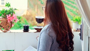 A person sitting on a bench reading a book, with a potted plant and a cup on the table. - Hoai Huong Homestay (Lam Vien - Da Lat)