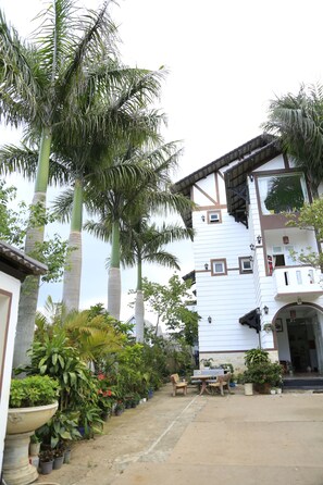A courtyard with a white building, palm trees, and potted plants. - Hoai Huong Homestay (Lam Vien - Da Lat)