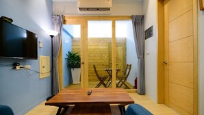 A compact room with a wooden dining table, two chairs, a TV mounted on the wall, and a sliding wooden door leading to an outdoor area. - Summer Sea Hostel (Magong)
