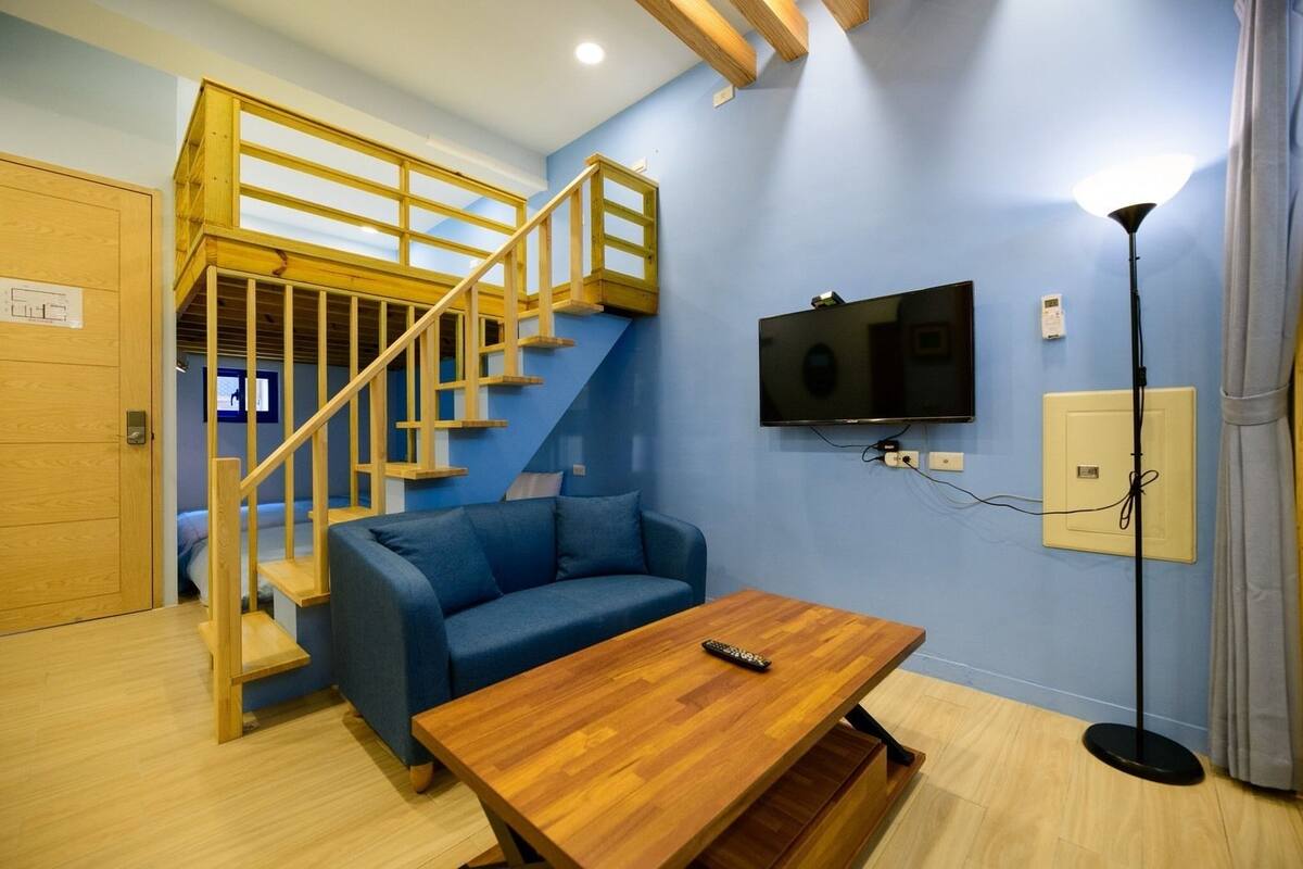 Una habitación con un sofá azul, una mesa de centro de madera y un televisor en la pared.