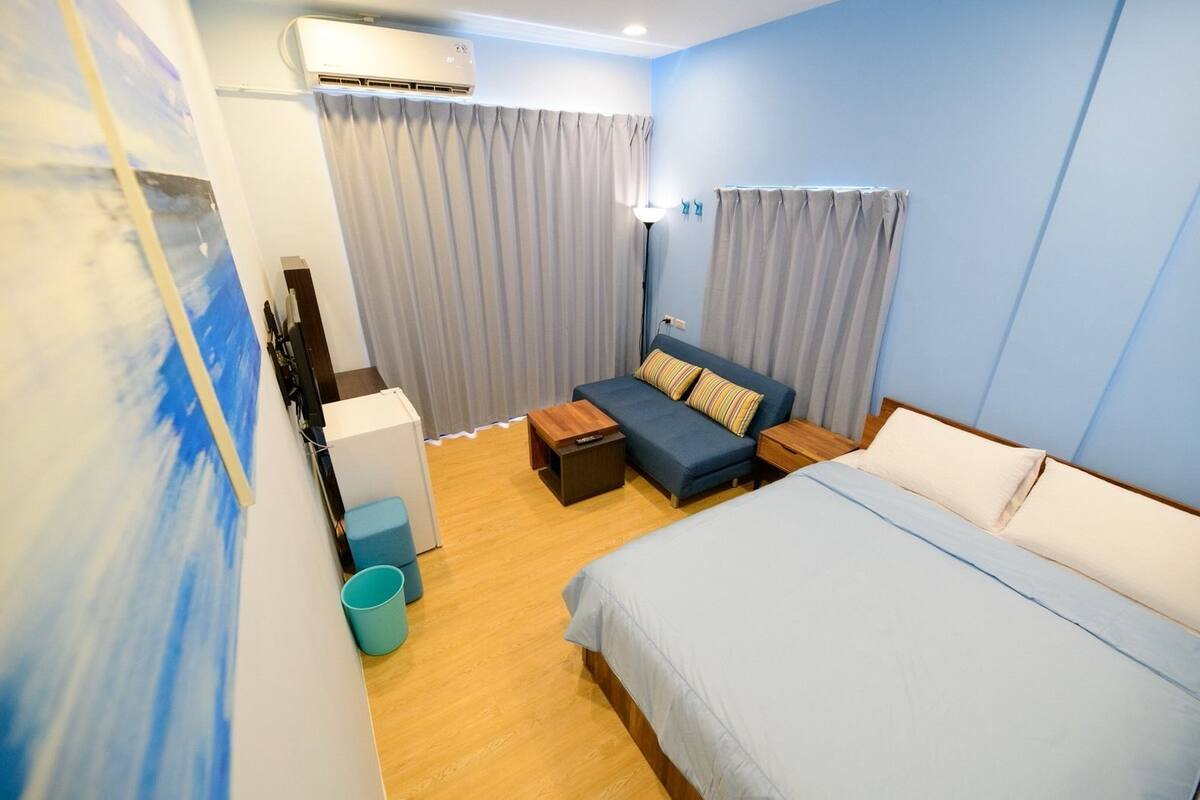 Una habitación de hotel con cama, sofá, escritorio y un cesto de basura.