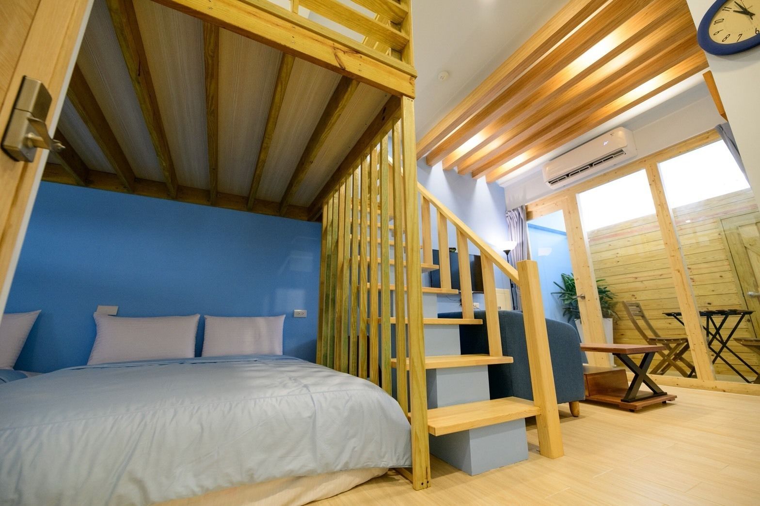 A bedroom with a bed, a wooden staircase, and a view of the outside.