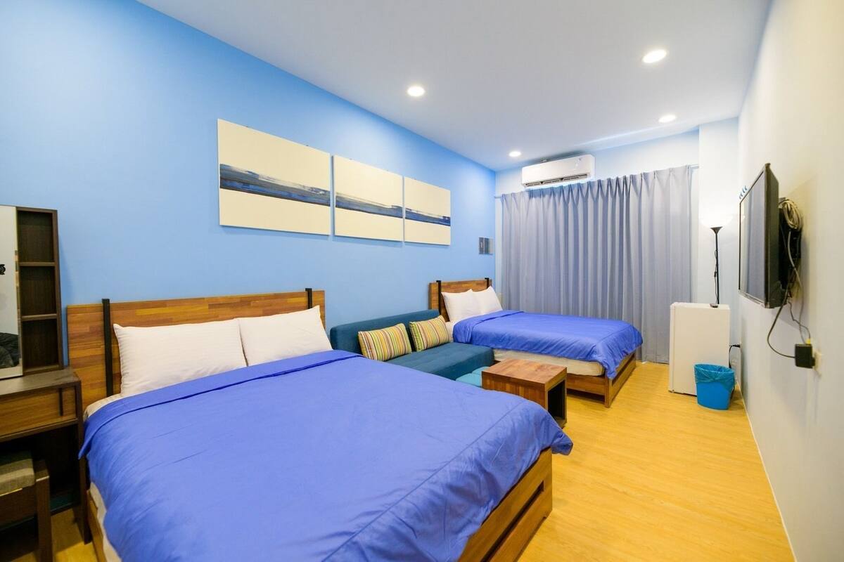 Habitación de hotel con dos camas, un sofá, una mesita pequeña, un equipo de aire acondicionado y un televisor.