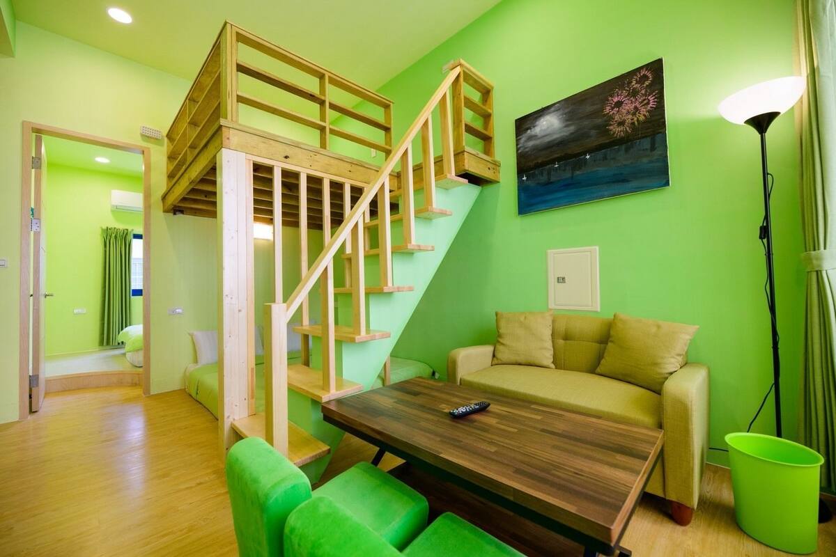 Una habitación con una escalera de madera, un sofá, una mesa y un cuadro en la pared.