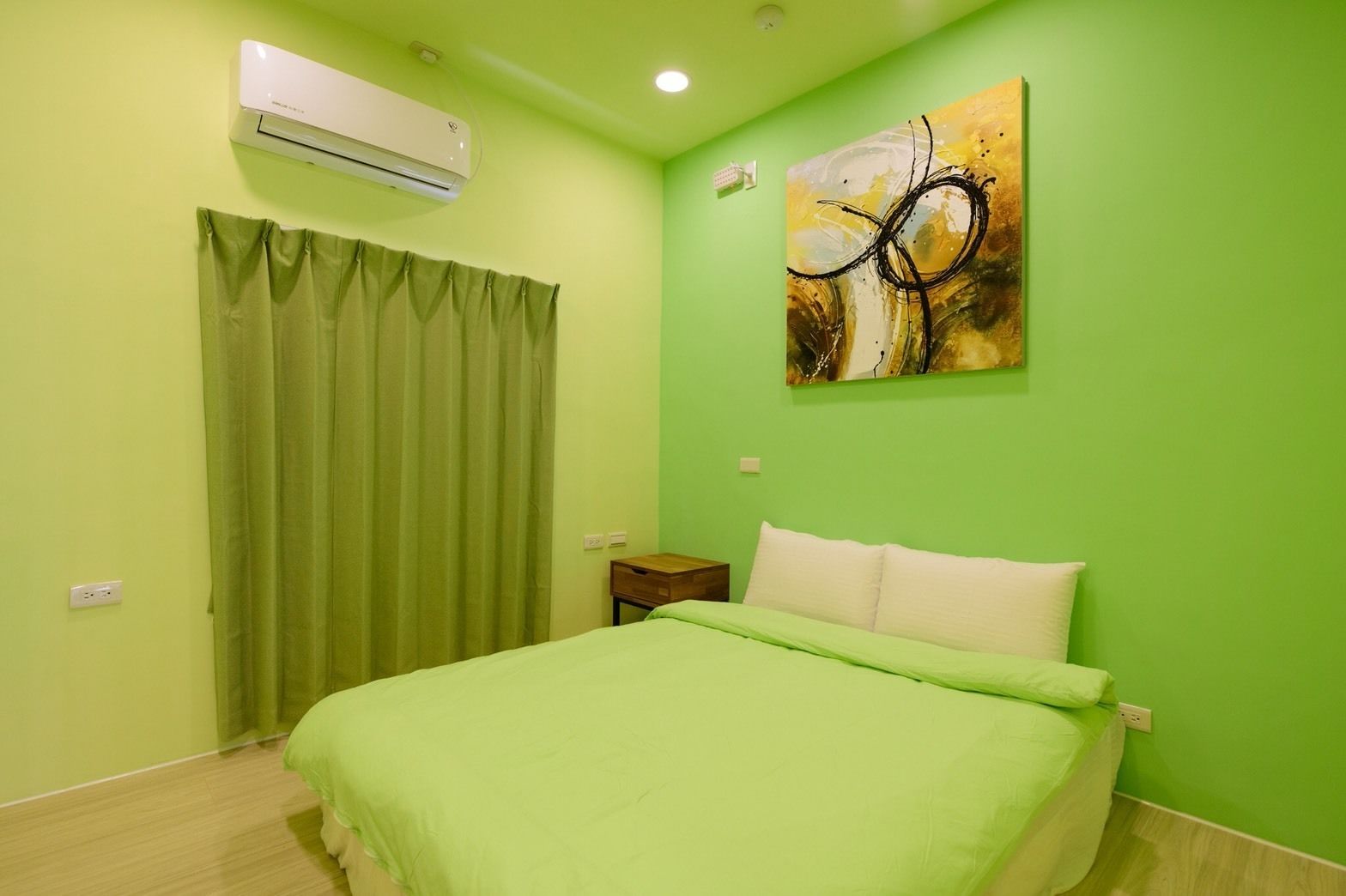 A room with a bed, a nightstand, an air conditioner, a painting, and a green curtain.