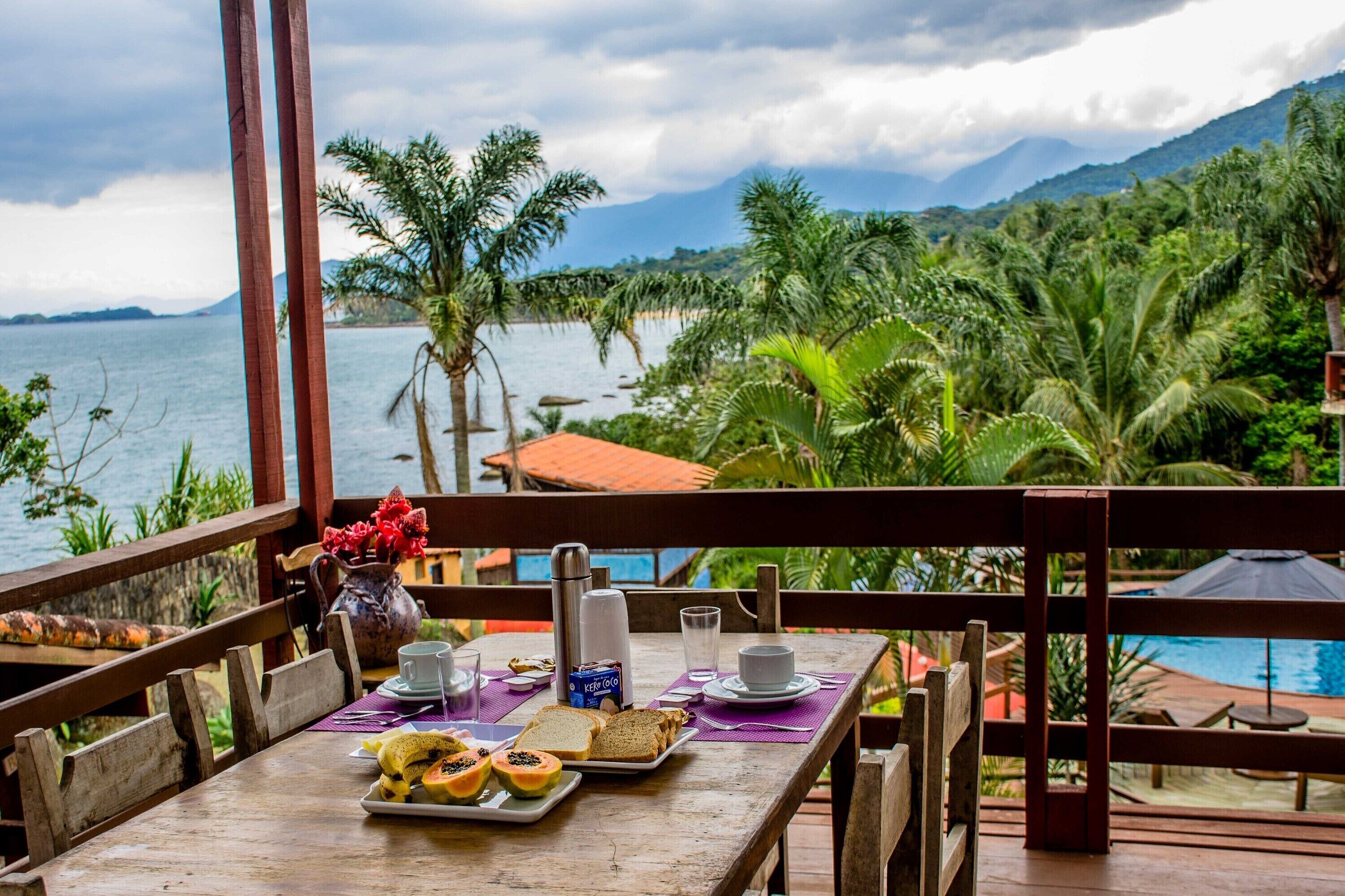 A wooden table with breakfast items, a view of a beach, and a pool.