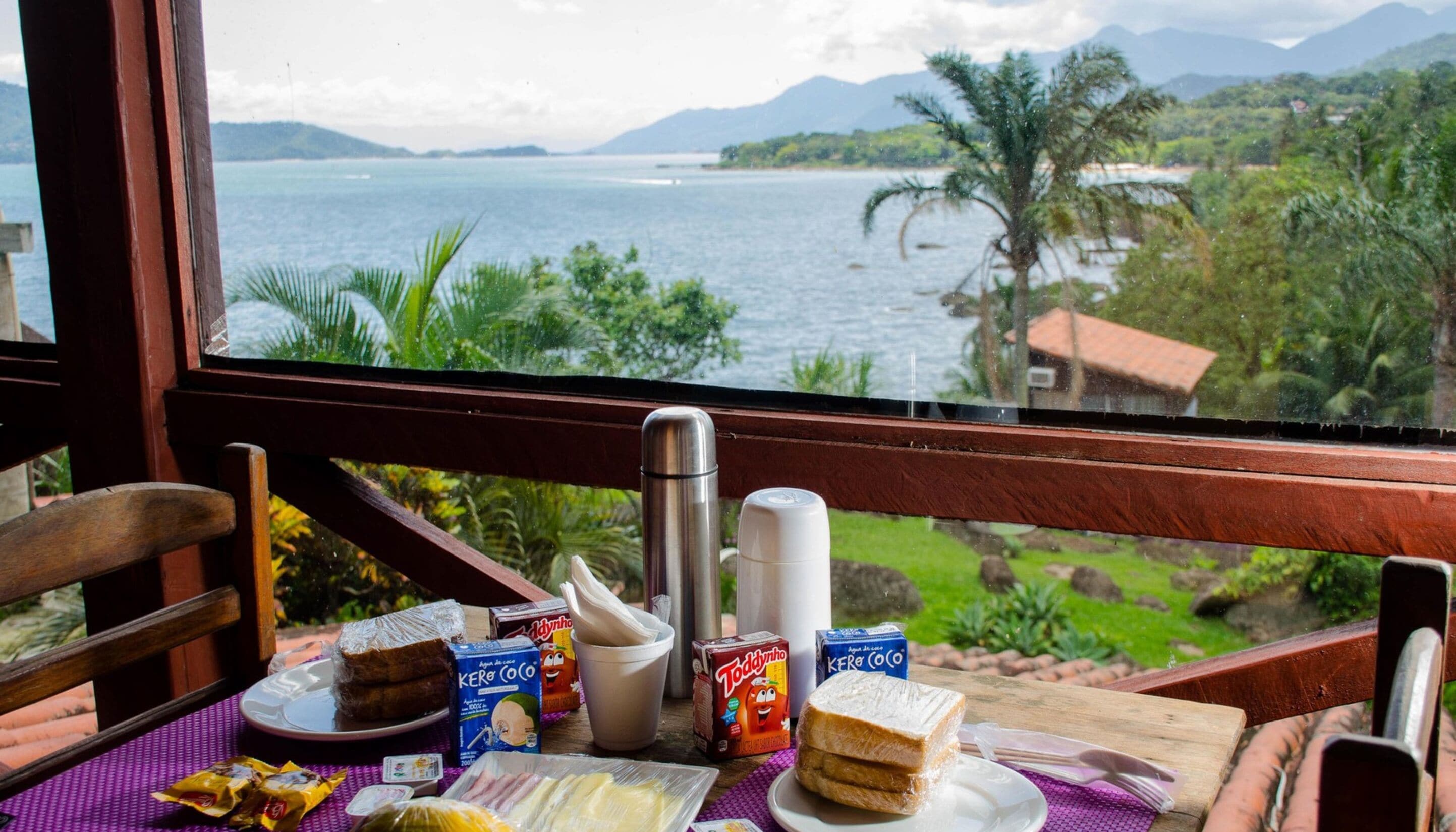 Una mesa de desayuno con comida y un termo, con vistas a un paisaje escénico de un lago y montañas.