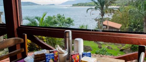 Una mesa de desayuno con comida y un termo, con vistas a un paisaje escénico de un lago y montañas.