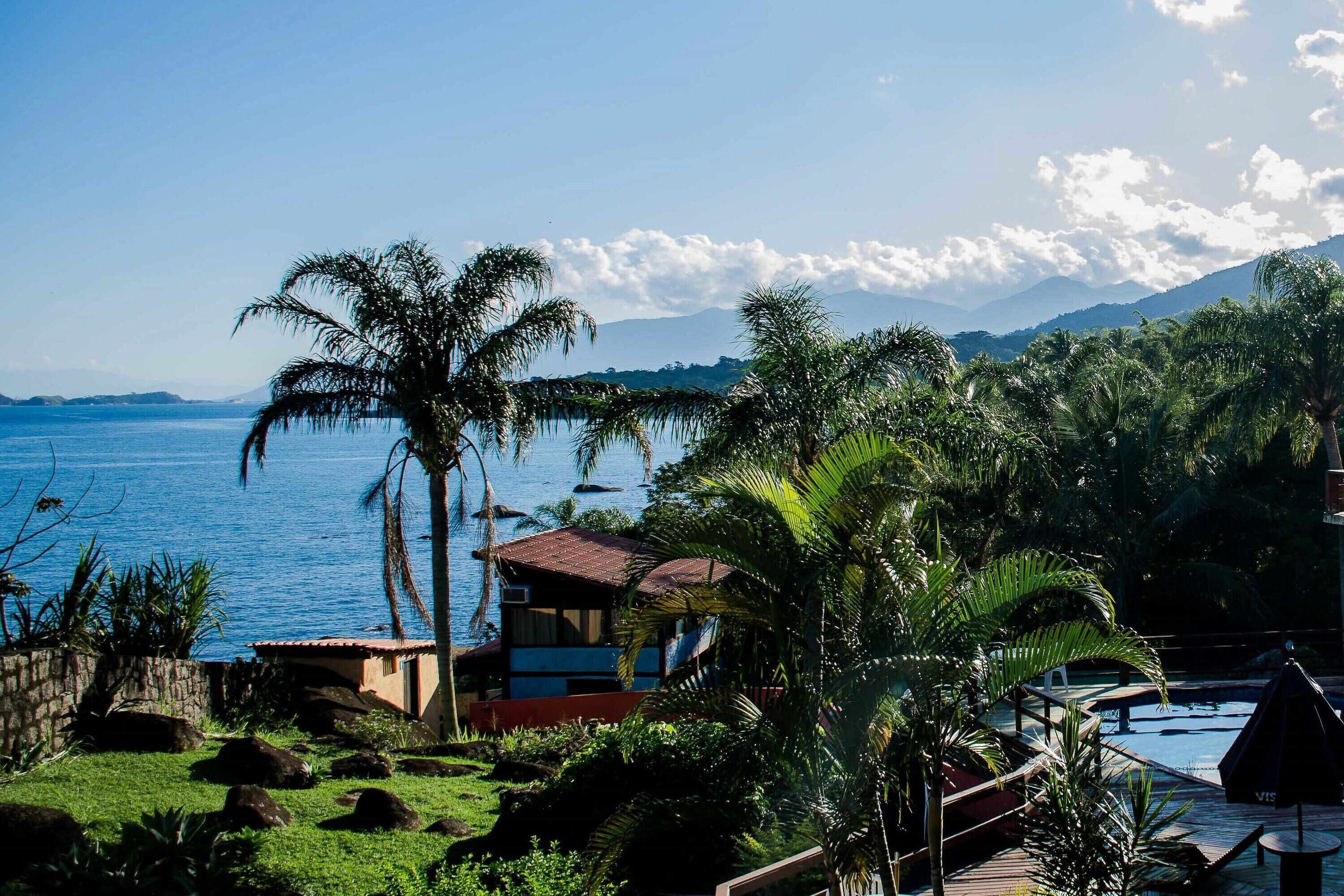 Un resort tropical con piscina, palmeras y vistas al océano y a las montañas.
