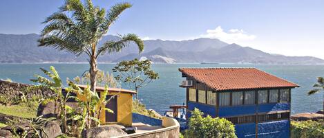 A coastal building with a red roof overlooking a body of water and mountains.