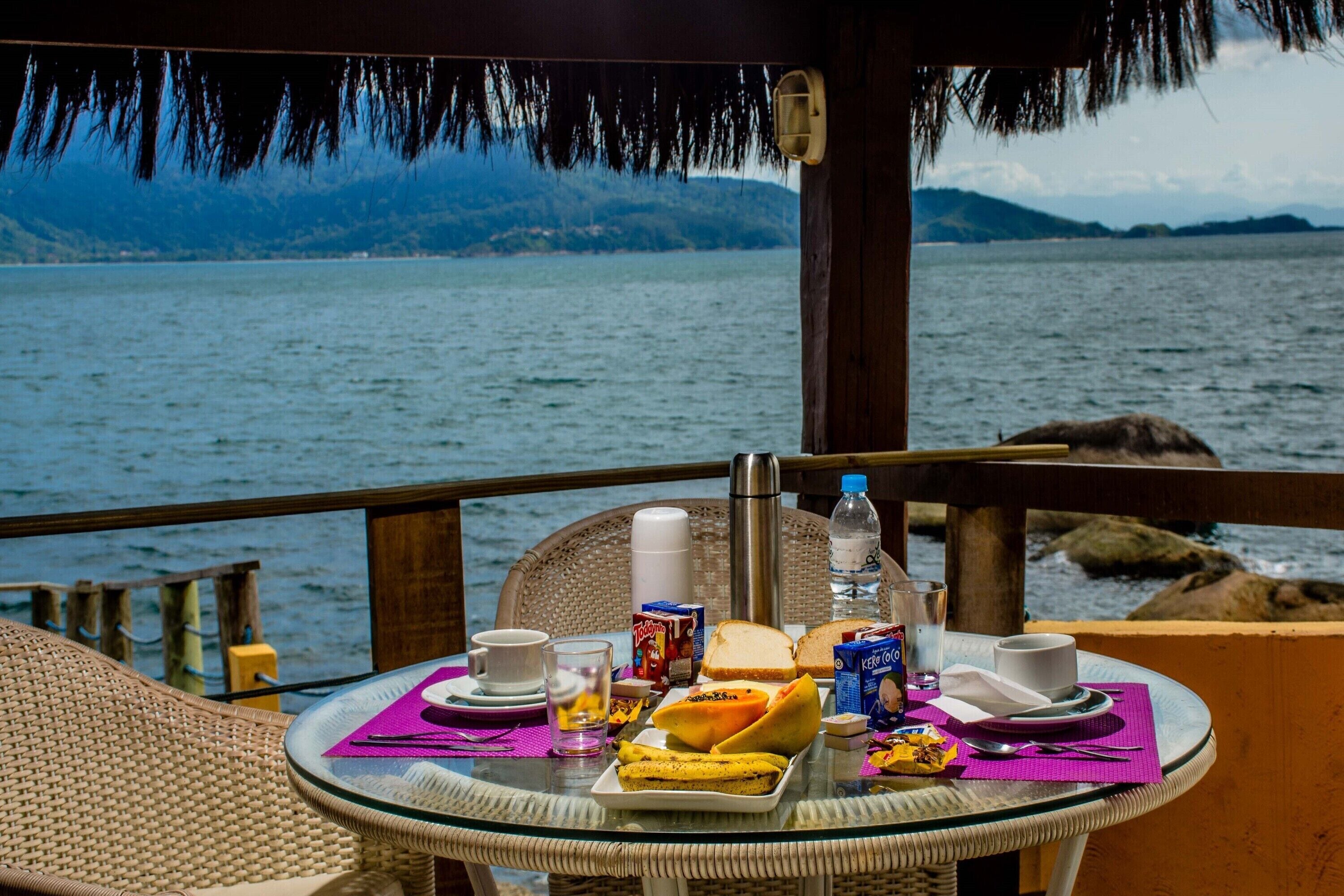 Taula de dinar amb menjar per esmorzar, una ampolla d'aigua i vista al mar i a les muntanyes.