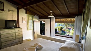 Ein Schlafzimmer mit Bett, Kommode, Fernseher und einem Fenster mit Vorhängen.